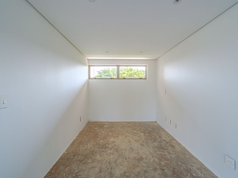 An empty, unfinished bedroom space featuring clean white walls, recessed ceiling lighting, and a horizontal clerestory window, awaiting final flooring installation.