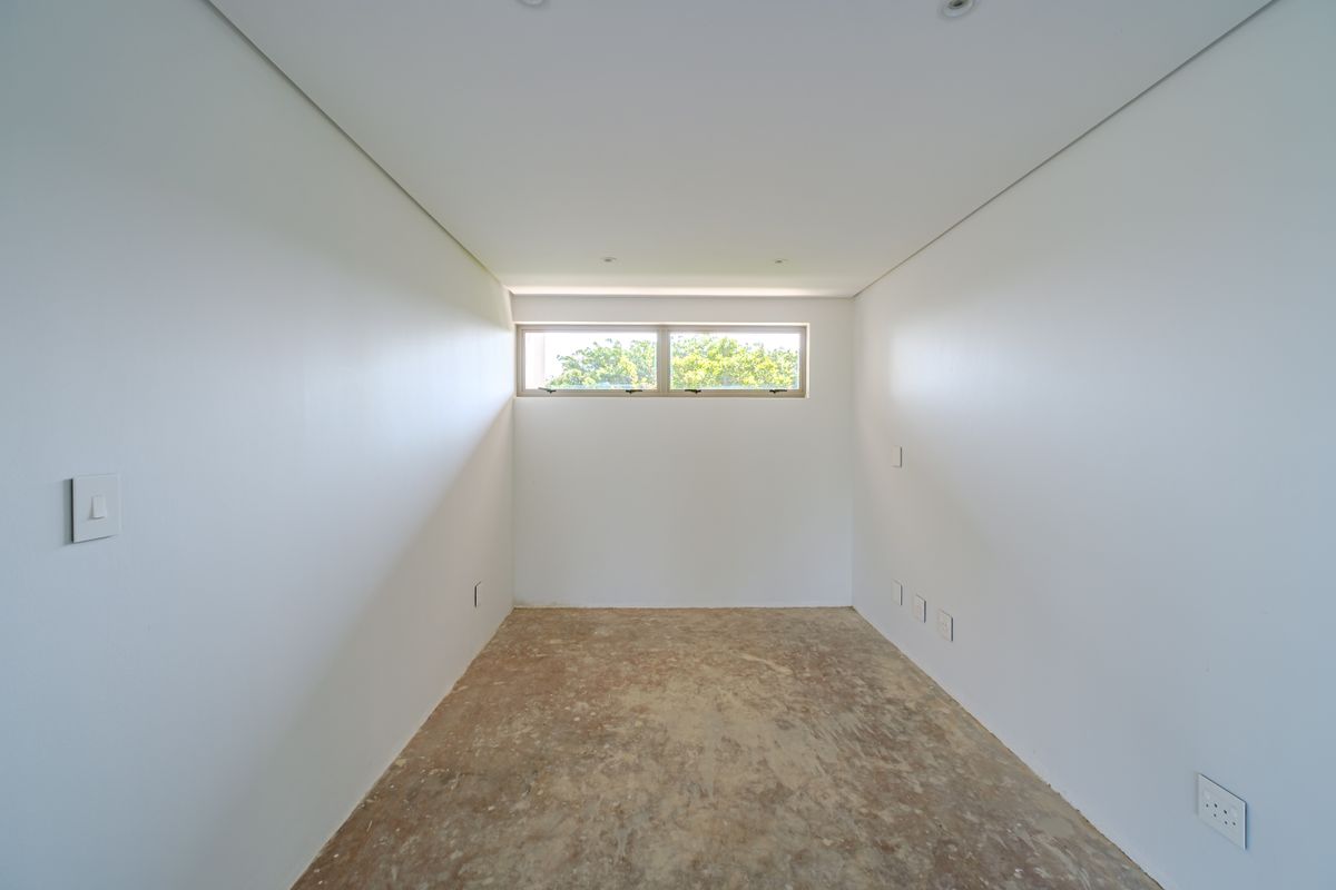 An empty, unfinished bedroom space featuring clean white walls, recessed ceiling lighting, and a horizontal clerestory window, awaiting final flooring installation.