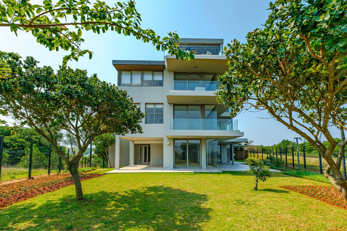 Rear view of a modern multi-story penthouse featuring tiered balconies with glass balustrades, sliding doors, and a well-maintained landscaped garden.