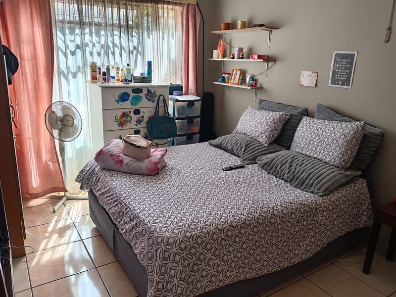 A bedroom featuring tiled flooring and wall-mounted shelving, with natural light entering through a large window.