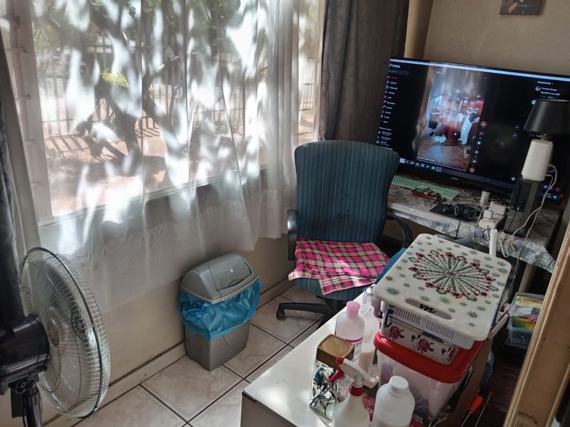 A living area featuring tiled flooring and a large window providing natural light, suitable for a comfortable seating or workspace arrangement.