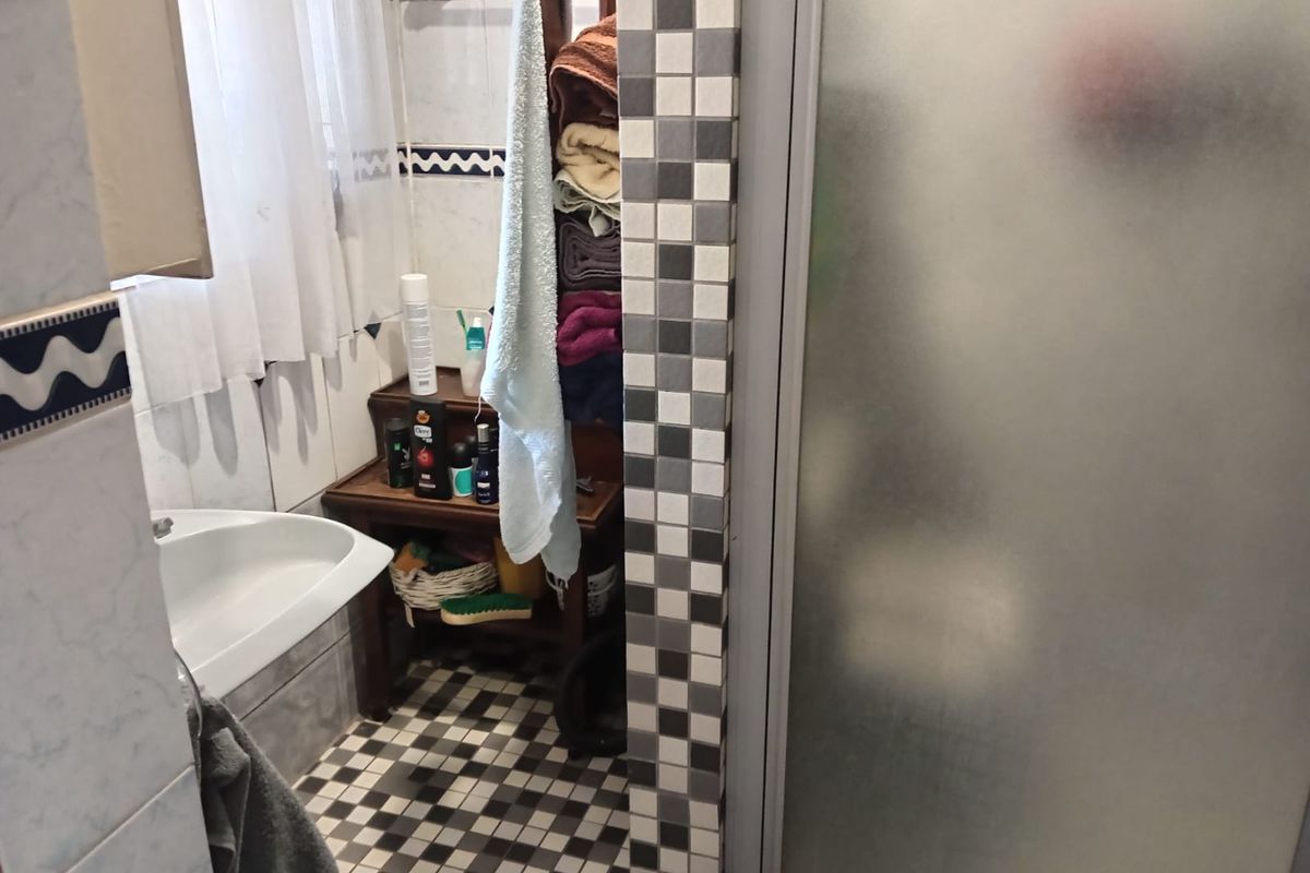 A functional bathroom featuring a shower enclosure, tiled walls, and a washbasin with a classic checkerboard floor pattern.