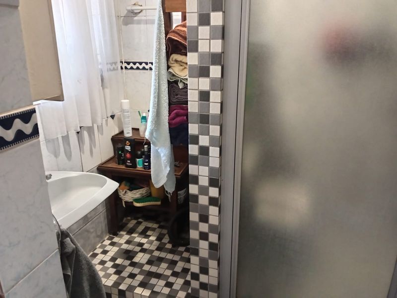 A functional bathroom featuring a shower enclosure, tiled walls, and a washbasin with a classic checkerboard floor pattern.