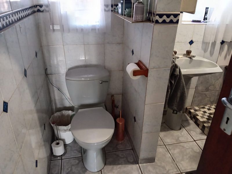 A dated bathroom featuring a standard toilet and pedestal washbasin with tiled walls and flooring, requiring cosmetic updates and minor repairs.