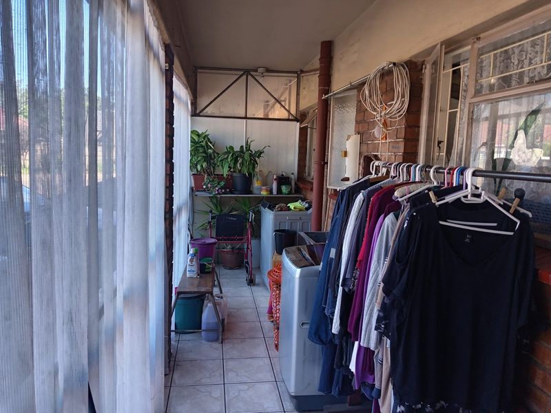 A covered balcony or patio area featuring tiled flooring and exposed brick walls, currently utilized as a laundry and utility space.