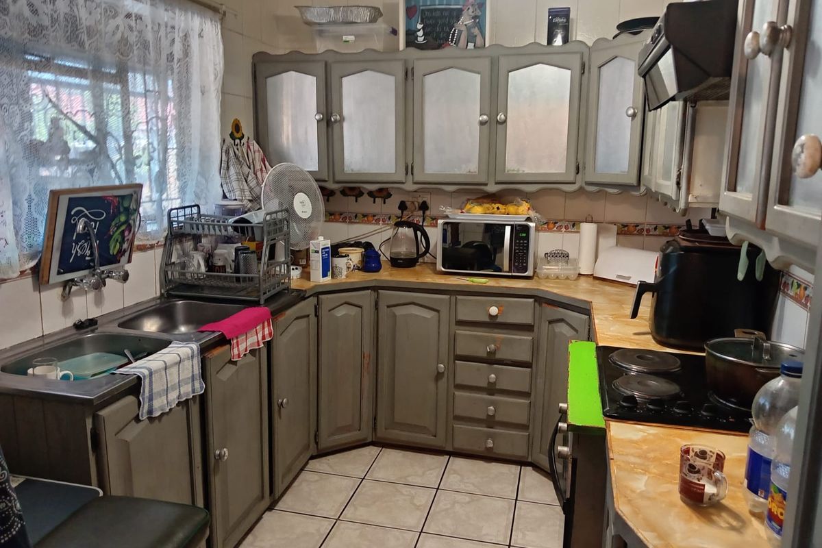 A functional kitchen featuring built-in cabinetry, a double basin sink, and a ceramic hob with an extractor fan, requiring cosmetic updates.