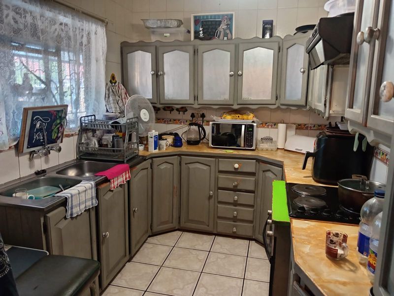 A functional kitchen featuring built-in cabinetry, a double basin sink, and a ceramic hob with an extractor fan, requiring cosmetic updates.
