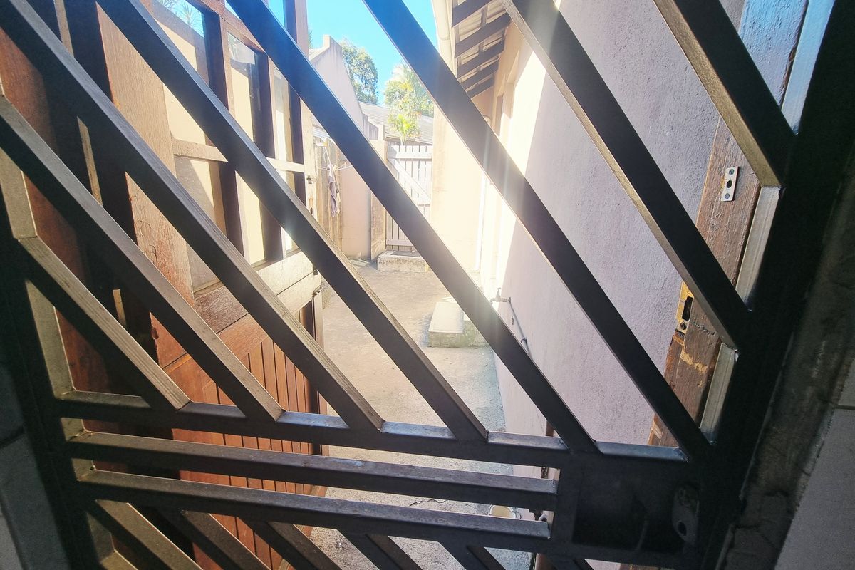 A view of the rear exterior area featuring a security gate, concrete paving, and an external water tap.