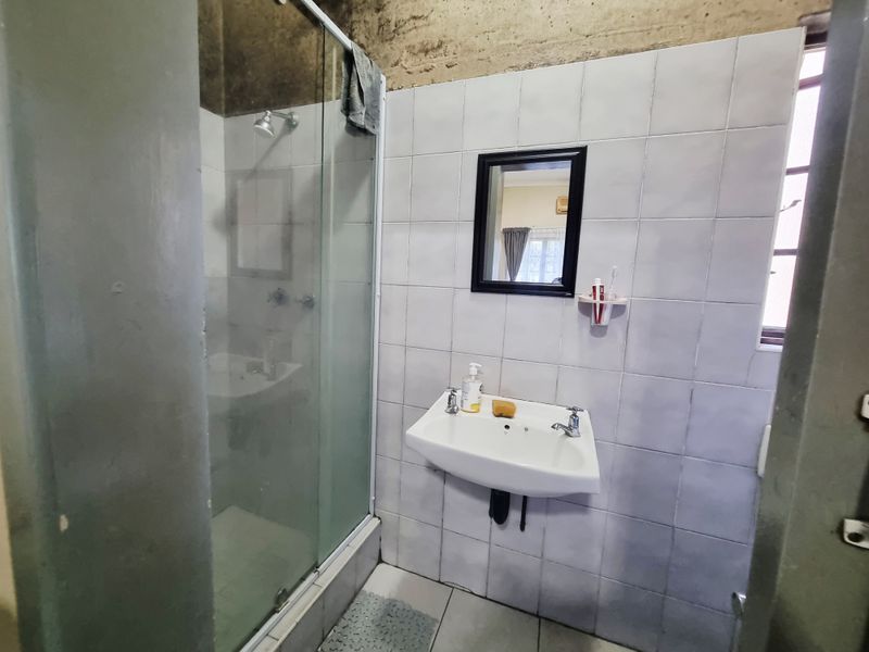 A functional bathroom featuring a glass shower enclosure, wall-mounted basin, and tiled walls, with an unfinished concrete upper wall section.