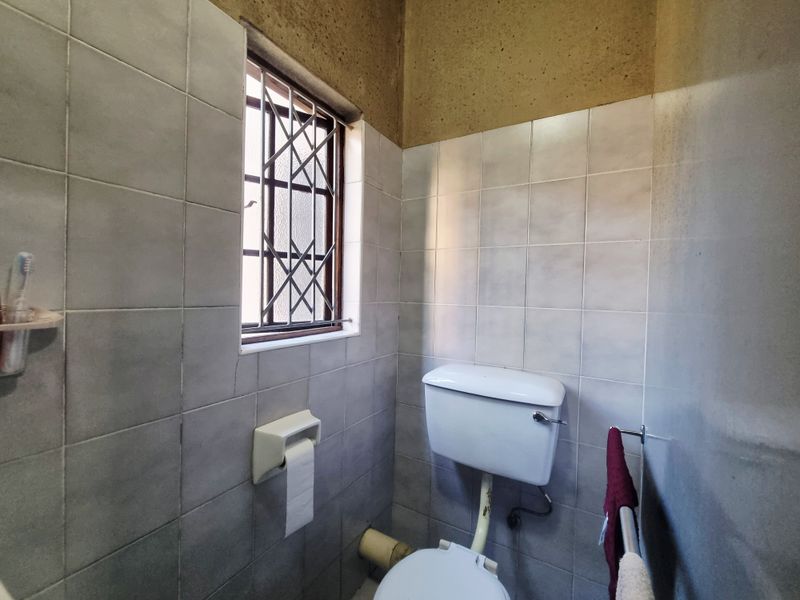 A compact bathroom featuring tiled walls, a standard toilet, and a window with security bars. The upper wall area requires finishing.