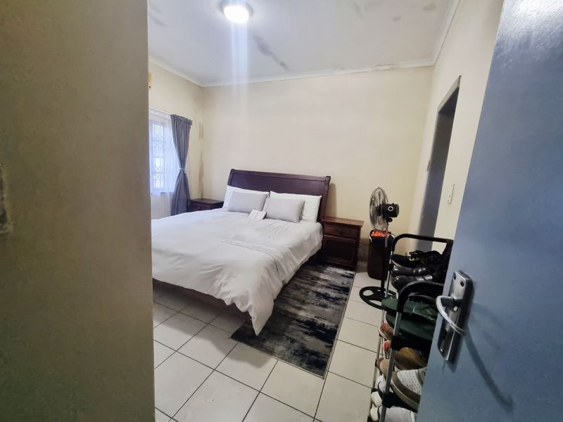 A bedroom featuring tiled flooring and a window with security bars, showing signs of ceiling and wall wear that would benefit from cosmetic updates.