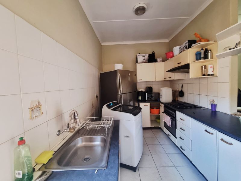 A functional kitchen featuring built-in cabinetry, a stainless steel sink, gas hob, and oven with tiled splashbacks and flooring.