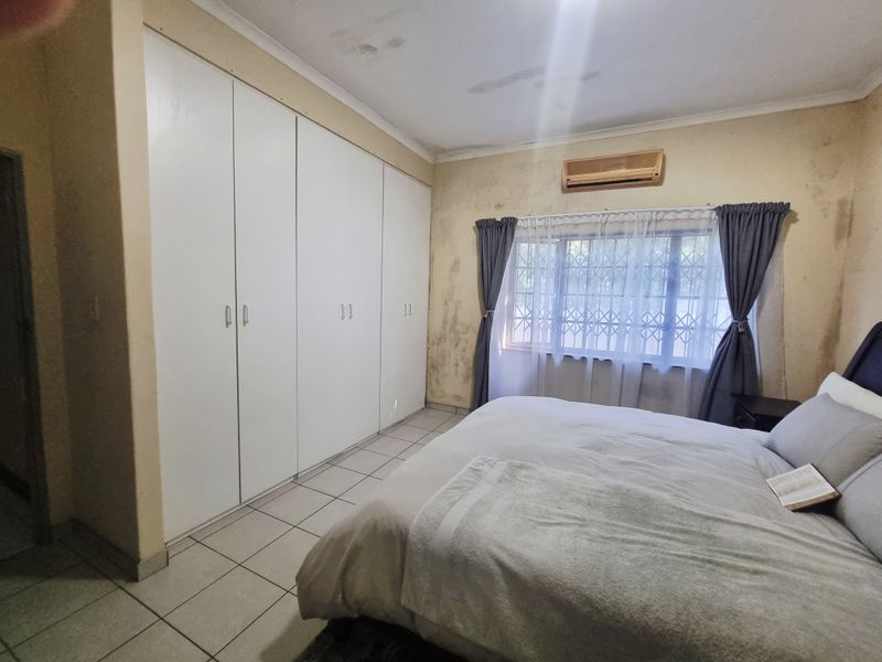 Bedroom featuring built-in cupboards, tiled flooring, and an air conditioning unit. The room requires cosmetic attention to the walls and ceiling.