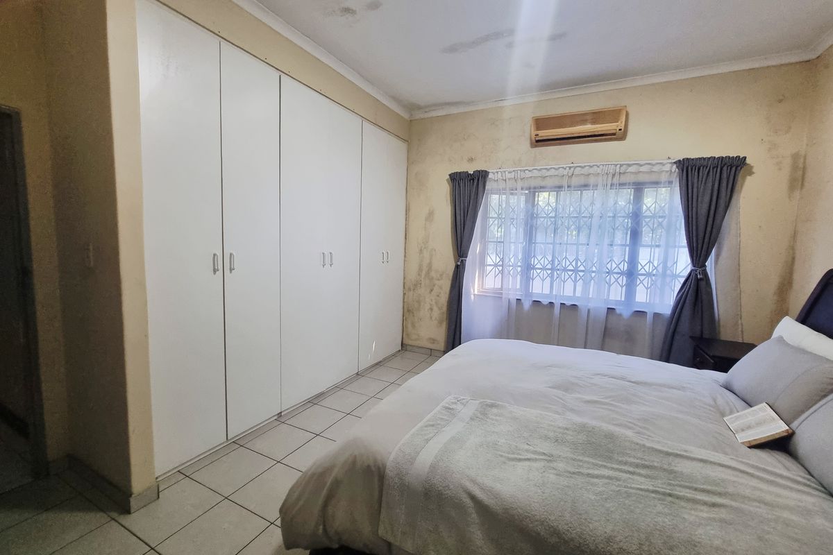 Bedroom featuring built-in cupboards, tiled flooring, and an air conditioning unit. The room requires cosmetic attention to the walls and ceiling.