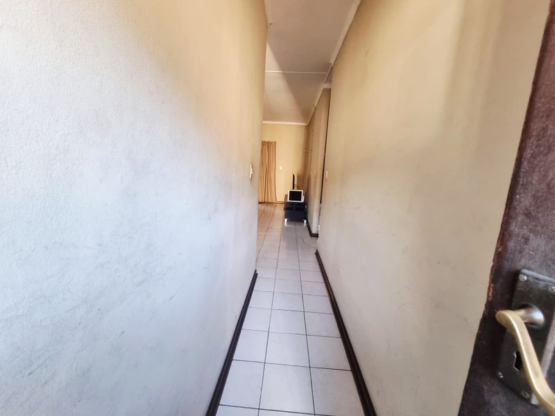 A narrow residential hallway featuring tiled flooring and plain walls, leading towards an open living area.