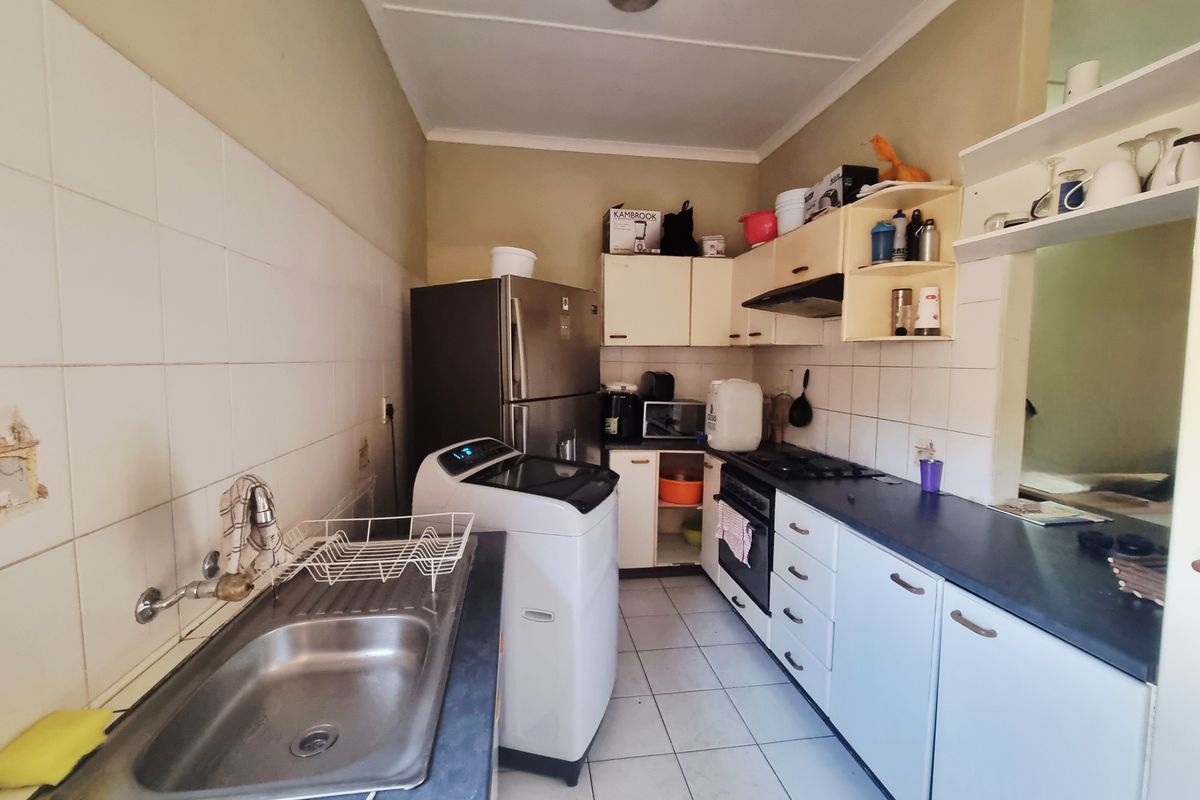 A functional kitchen featuring built-in cabinetry, a gas hob, oven, and stainless steel sink with tiled splashbacks and flooring.