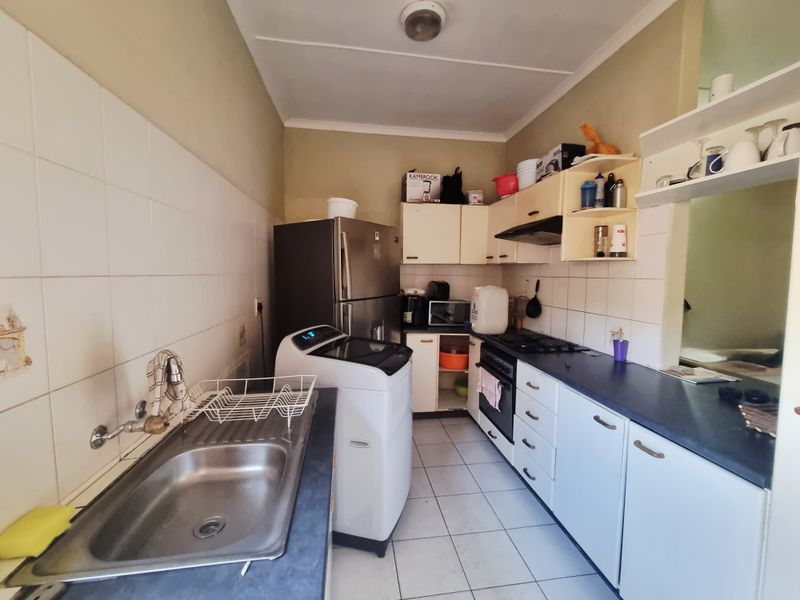 A functional kitchen featuring built-in cabinetry, a gas hob, oven, and stainless steel sink with tiled splashbacks and flooring.