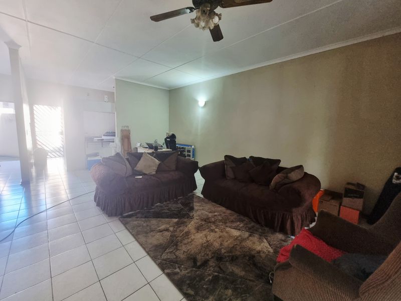 Spacious living area featuring tiled flooring, a ceiling fan, and neutral wall tones, offering a blank canvas for modern interior updates.