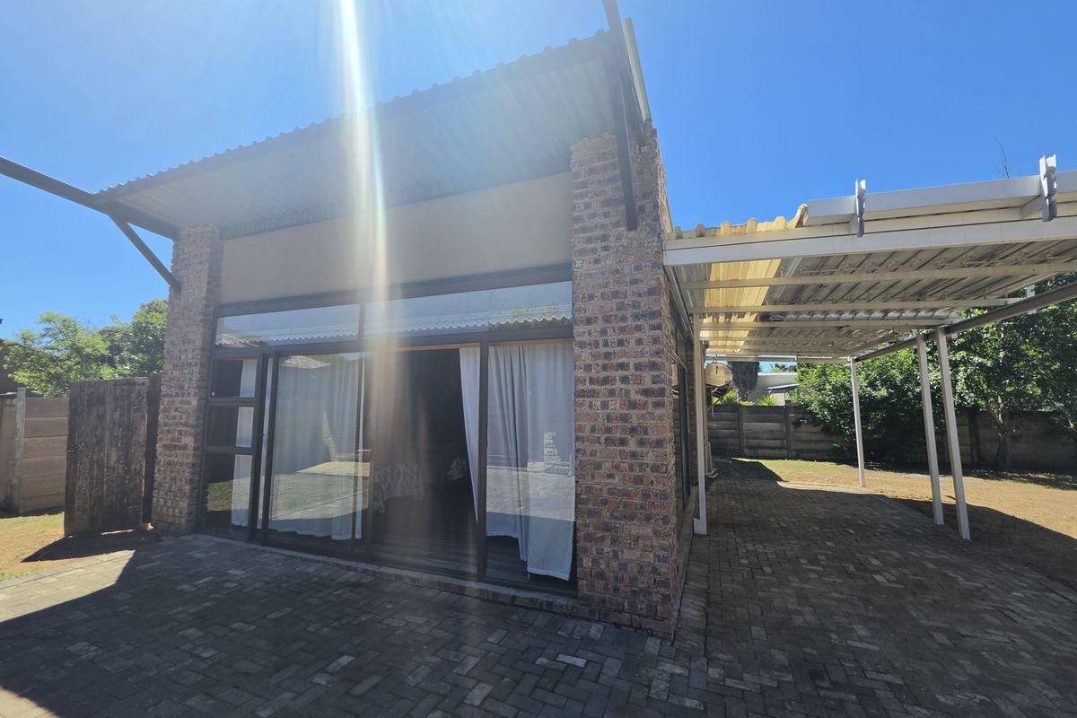 Rear exterior view featuring a face brick facade, large sliding glass doors, a paved patio area, and a covered carport structure.