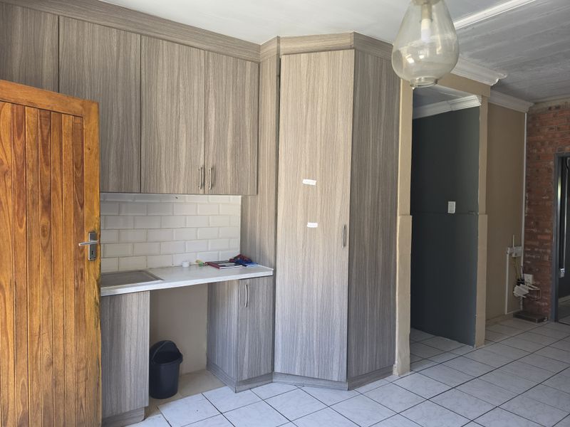 A functional scullery area featuring wood-look cabinetry, subway tile backsplash, and tiled flooring, offering practical storage and prep space.