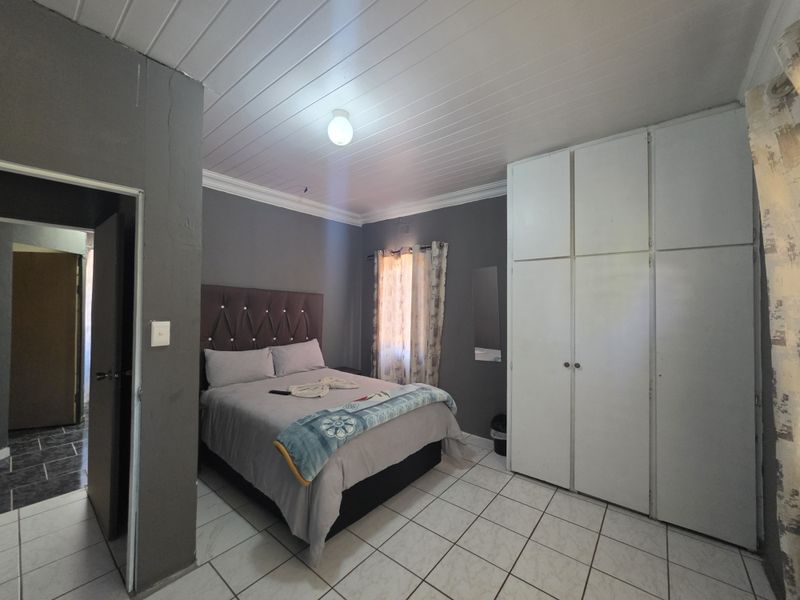 A bedroom featuring built-in cupboards, tiled flooring, and a tongue and groove ceiling, offering a functional space with potential for cosmetic updates.