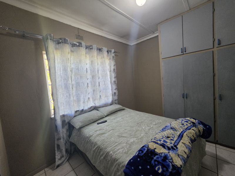 A compact bedroom featuring built-in cupboards, tiled flooring, and a window with curtaining.
