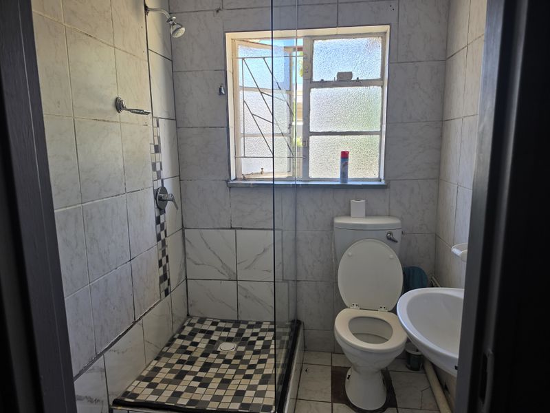 A compact bathroom featuring a walk-in shower with glass screen, pedestal basin, and toilet, finished with tiled walls and flooring.