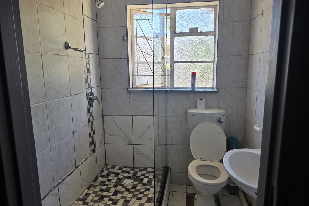 A compact bathroom featuring a walk-in shower with glass screen, pedestal basin, and toilet, finished with tiled walls and flooring.