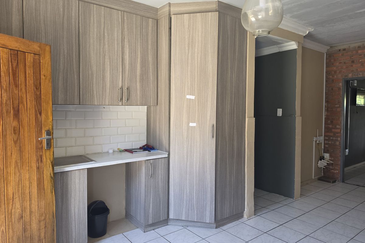 A kitchen area featuring modern wood-grain cabinetry, subway tile backsplash, and ceramic floor tiles, adjacent to an exposed brick wall and transition space.