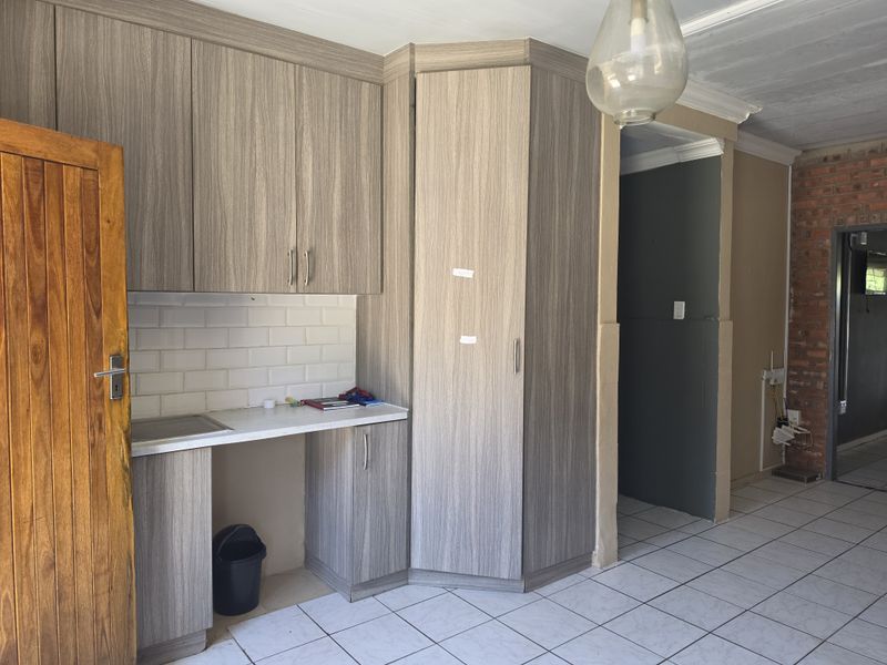 A kitchen area featuring modern wood-grain cabinetry, subway tile backsplash, and ceramic floor tiles, adjacent to an exposed brick wall and transition space.