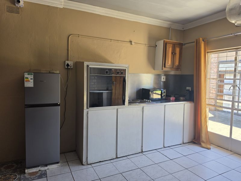 A functional kitchen area featuring built-in cabinetry, an integrated oven and hob, tiled flooring, and direct access to an outdoor patio area.