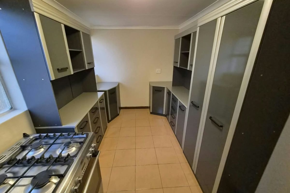 A functional kitchen featuring extensive built-in cabinetry, laminate countertops, and a gas stove, finished with neutral tiled flooring.