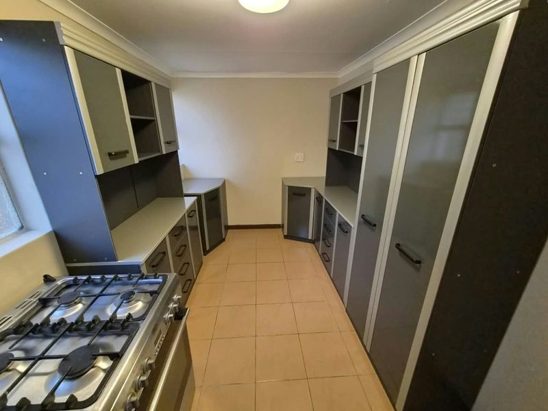 A functional kitchen featuring extensive built-in cabinetry, laminate countertops, and a gas stove, finished with neutral tiled flooring.