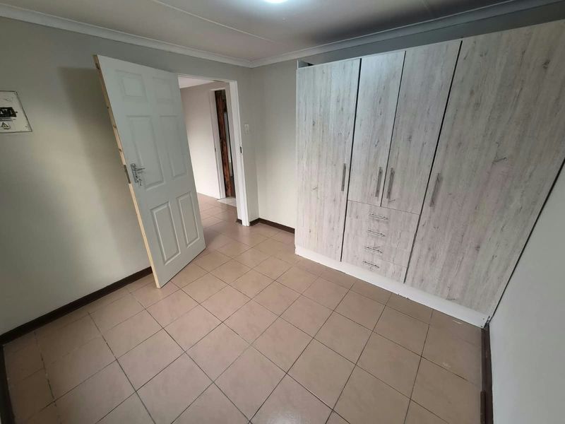 A vacant bedroom featuring neutral tiled flooring, built-in cupboards with a light wood finish, and access to an adjoining hallway.