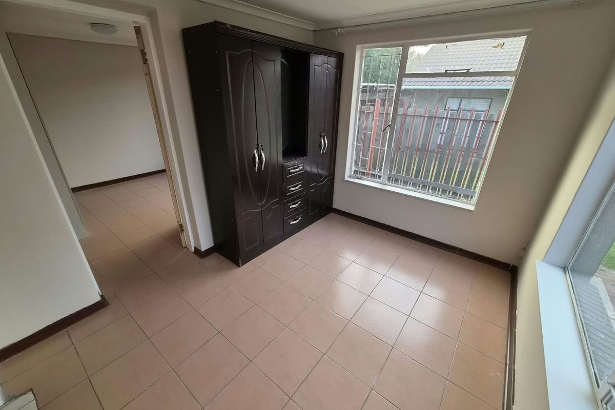A bedroom featuring tiled flooring, a built-in cupboard, and large windows allowing natural light, presenting a functional space ready for updates.