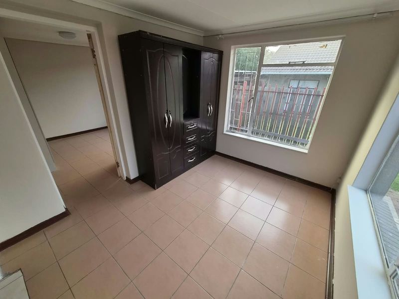 A bedroom featuring tiled flooring, a built-in cupboard, and large windows allowing natural light, presenting a functional space ready for updates.