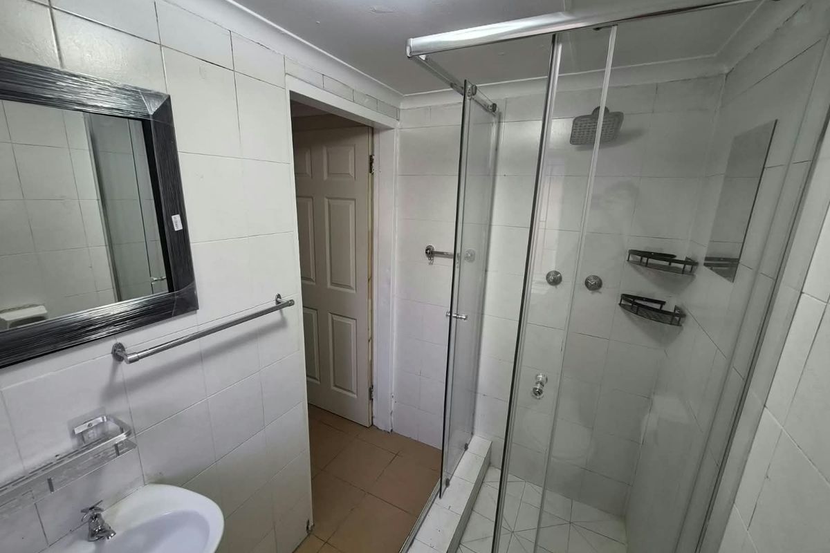 A functional bathroom featuring a glass shower enclosure, wall-mounted basin, and tiled finishes, offering a blank canvas for potential modernization and renovation.