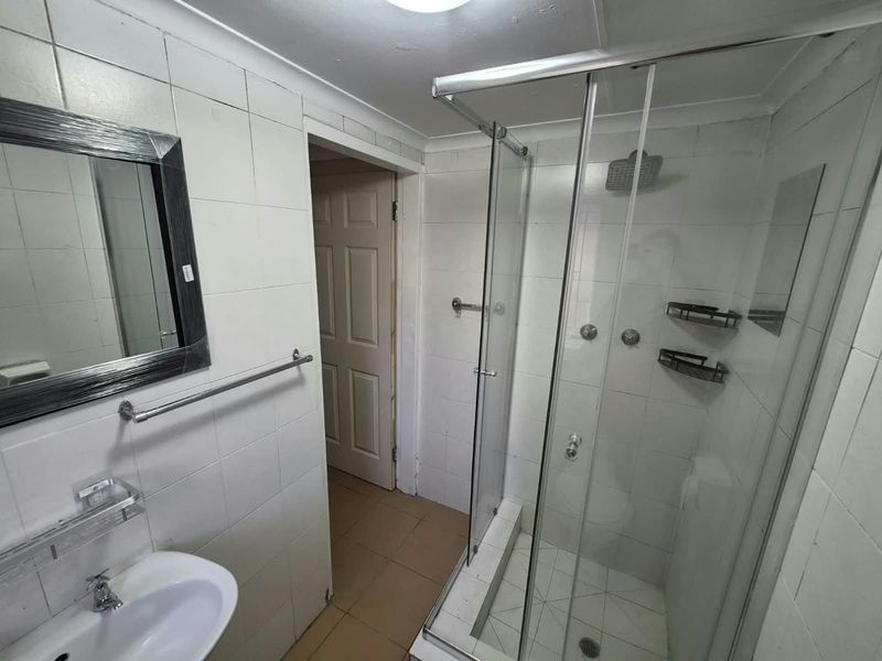 A functional bathroom featuring a glass shower enclosure, wall-mounted basin, and tiled finishes, offering a blank canvas for potential modernization and renovation.