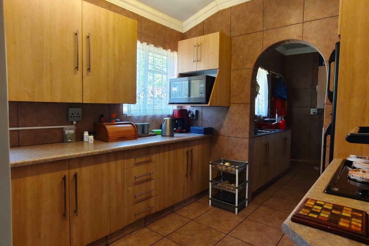 A functional kitchen featuring laminate cabinetry, tiled walls and flooring, and an arched entryway leading to a secondary prep area.