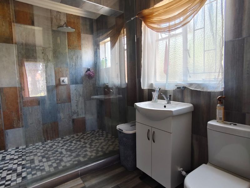 A bathroom featuring a walk-in shower with glass screen, vanity basin, and toilet, finished with decorative wall and floor tiling.