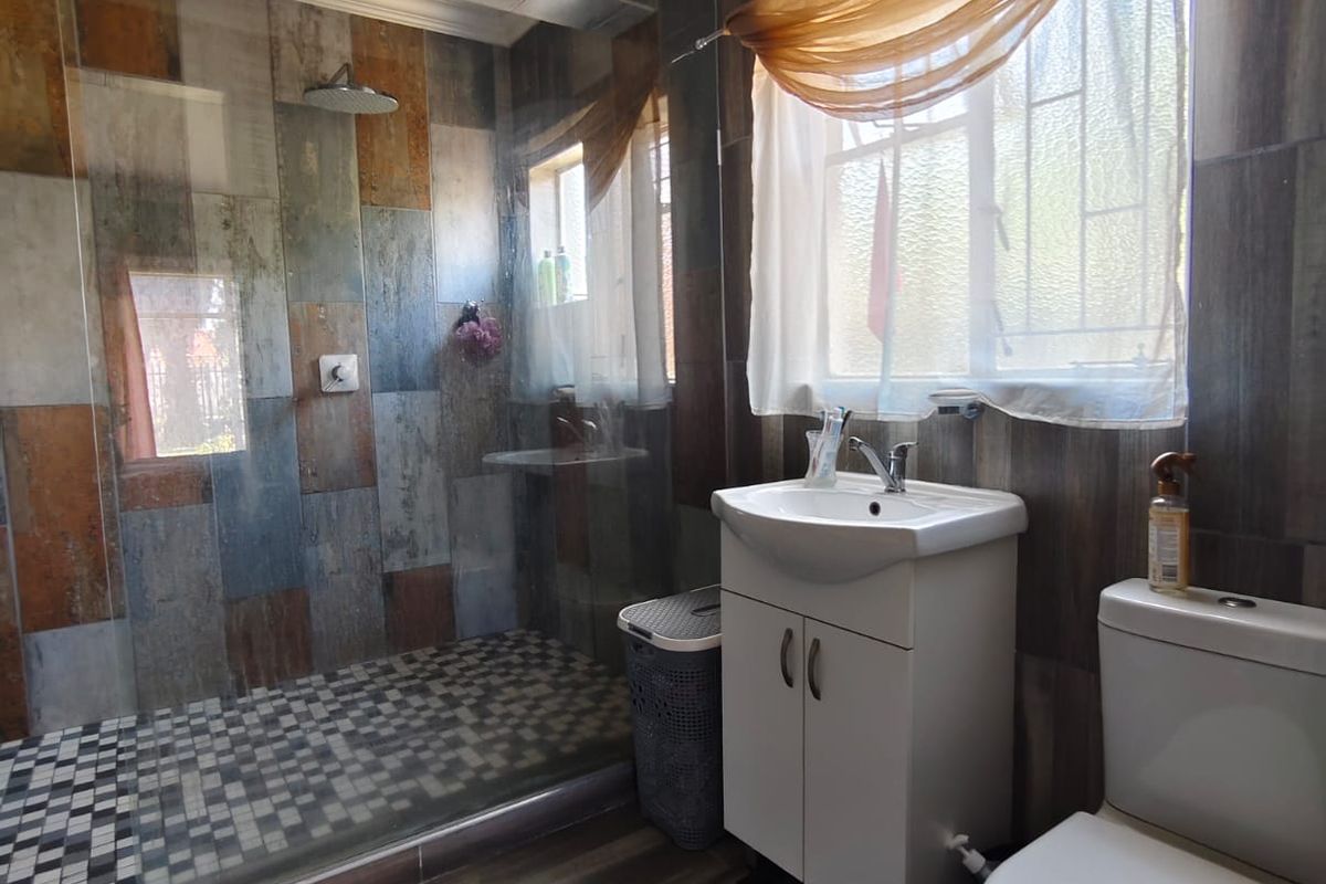 A bathroom featuring a walk-in shower with glass screen, vanity basin, and toilet, finished with decorative wall and floor tiling.