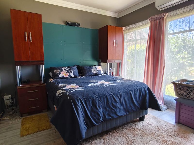 A bedroom featuring laminate flooring, built-in cupboards, and an air conditioning unit, with large windows allowing for natural light.