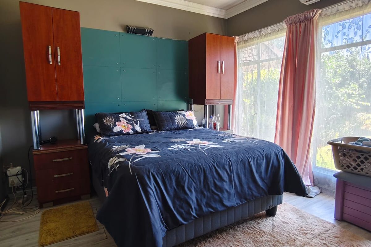 A bedroom featuring laminate flooring, built-in cupboards, and an air conditioning unit, with large windows allowing for natural light.
