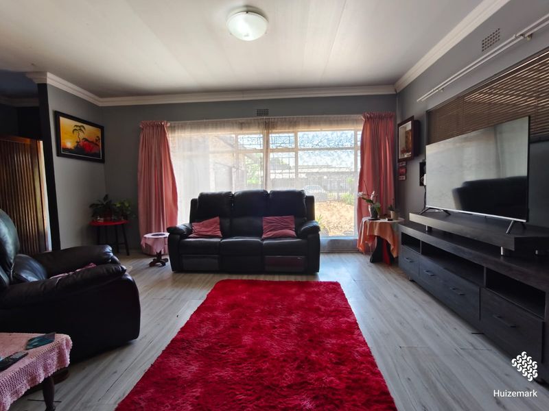 A spacious living room featuring light-toned laminate flooring, neutral grey walls, and a large window that provides ample natural light.
