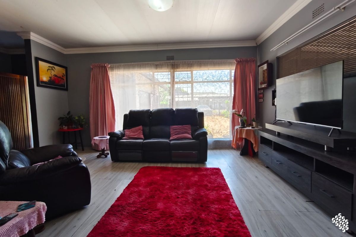 A spacious living room featuring light-toned laminate flooring, neutral grey walls, and a large window that provides ample natural light.