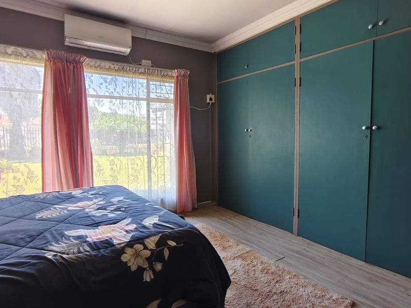 A bedroom featuring built-in cupboards, laminate flooring, and a wall-mounted air conditioning unit, offering a functional space with natural light.