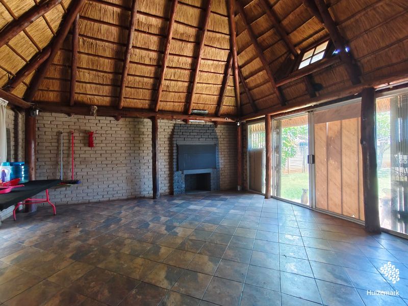 Spacious living area featuring a high thatched roof with exposed timber beams, a brick fireplace, and large sliding doors opening to the garden.
