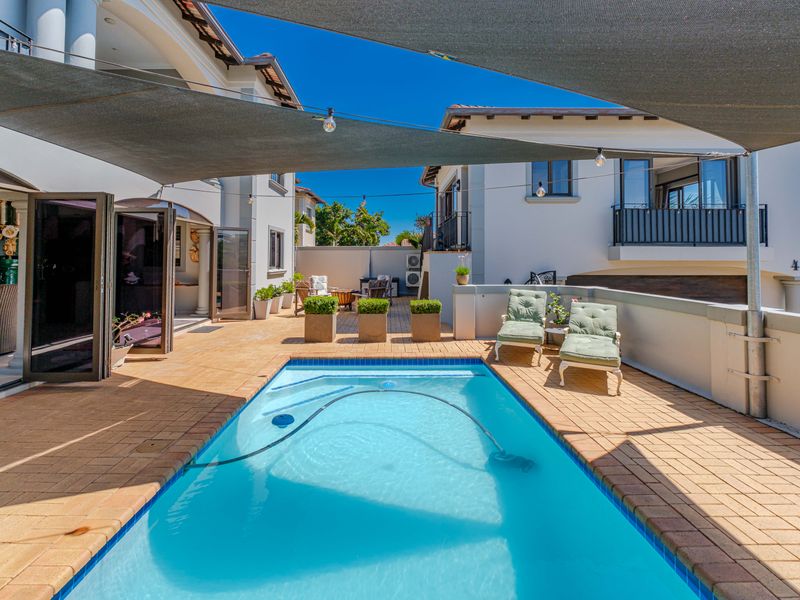 A well-maintained outdoor pool area featuring a paved patio, shade sail, and seamless access to the home through bi-fold doors.