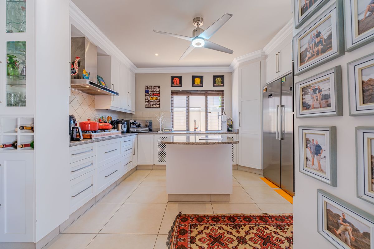A well-maintained kitchen featuring white cabinetry, granite countertops, a central island, tiled flooring, and a ceiling fan, offering a clean and functional workspace.
