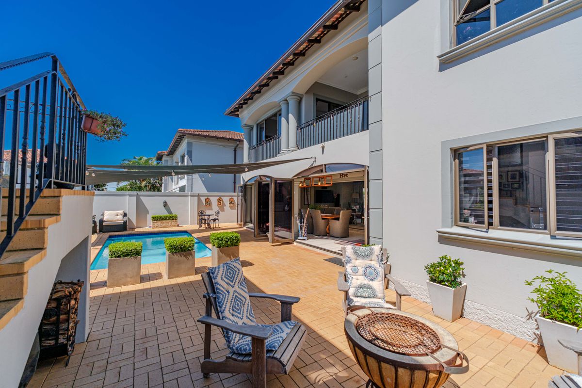 A well-maintained rear exterior featuring a paved patio, swimming pool, and a covered balcony with metal railings and folding glass doors.
